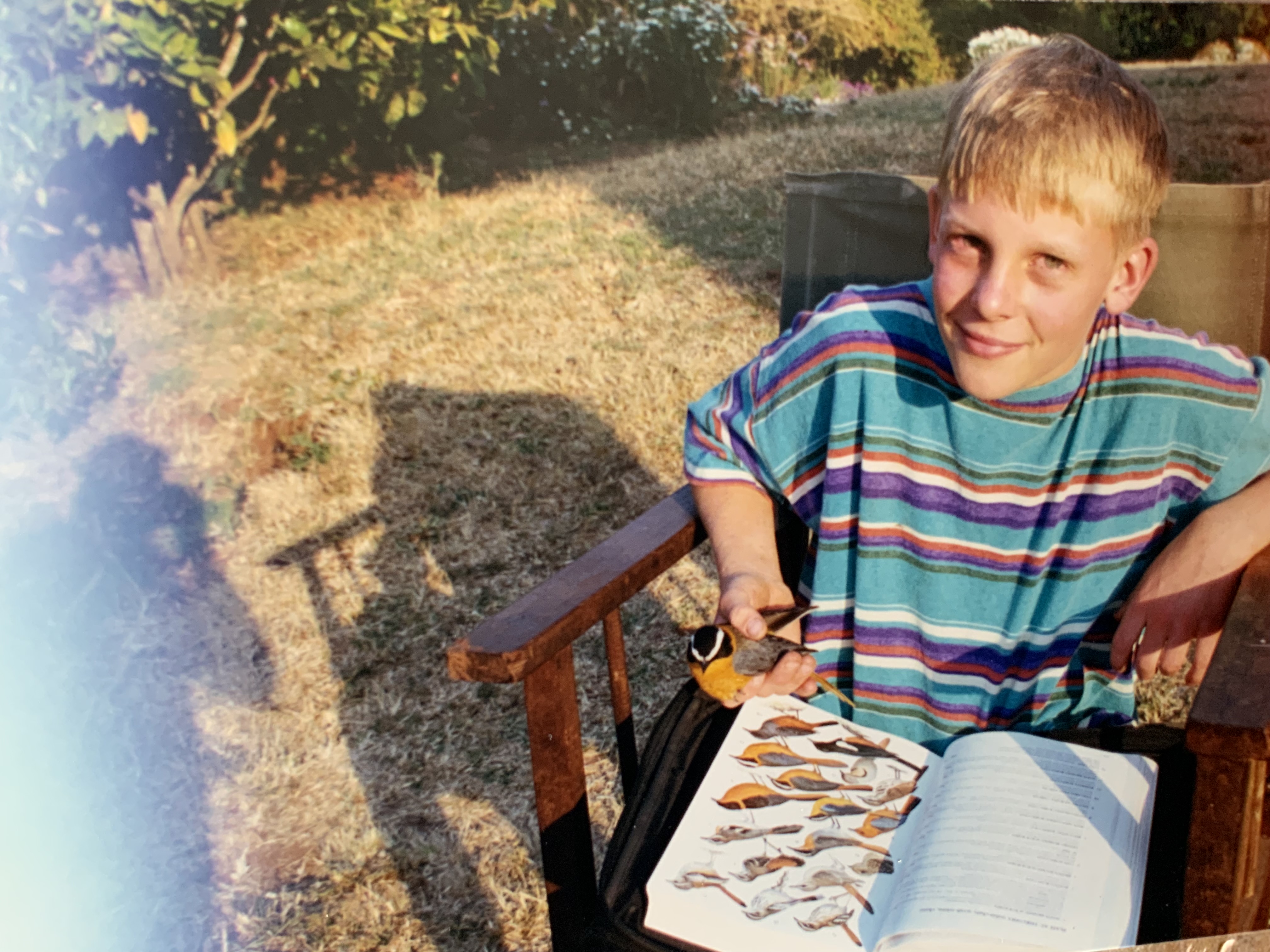 A young boy outdoors with a small bird and an open bird guide on his lap, East Africa, 1997