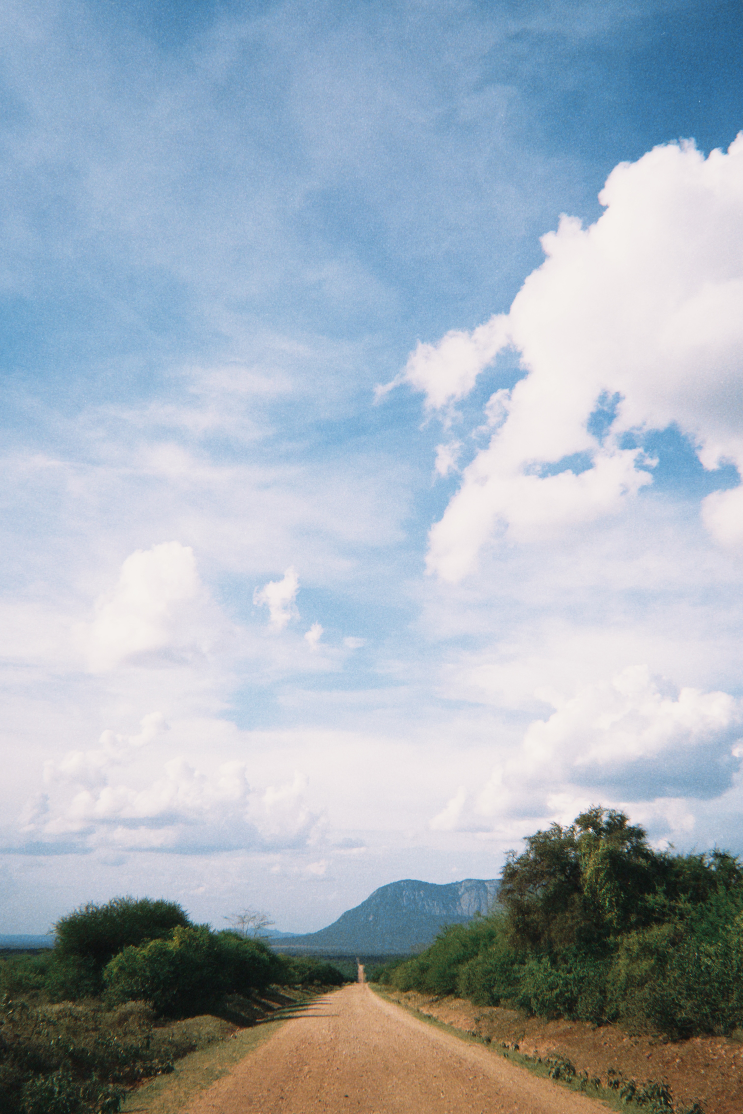 A long dirt road leading toward a distant mountain under a bright blue sky, Tanzania