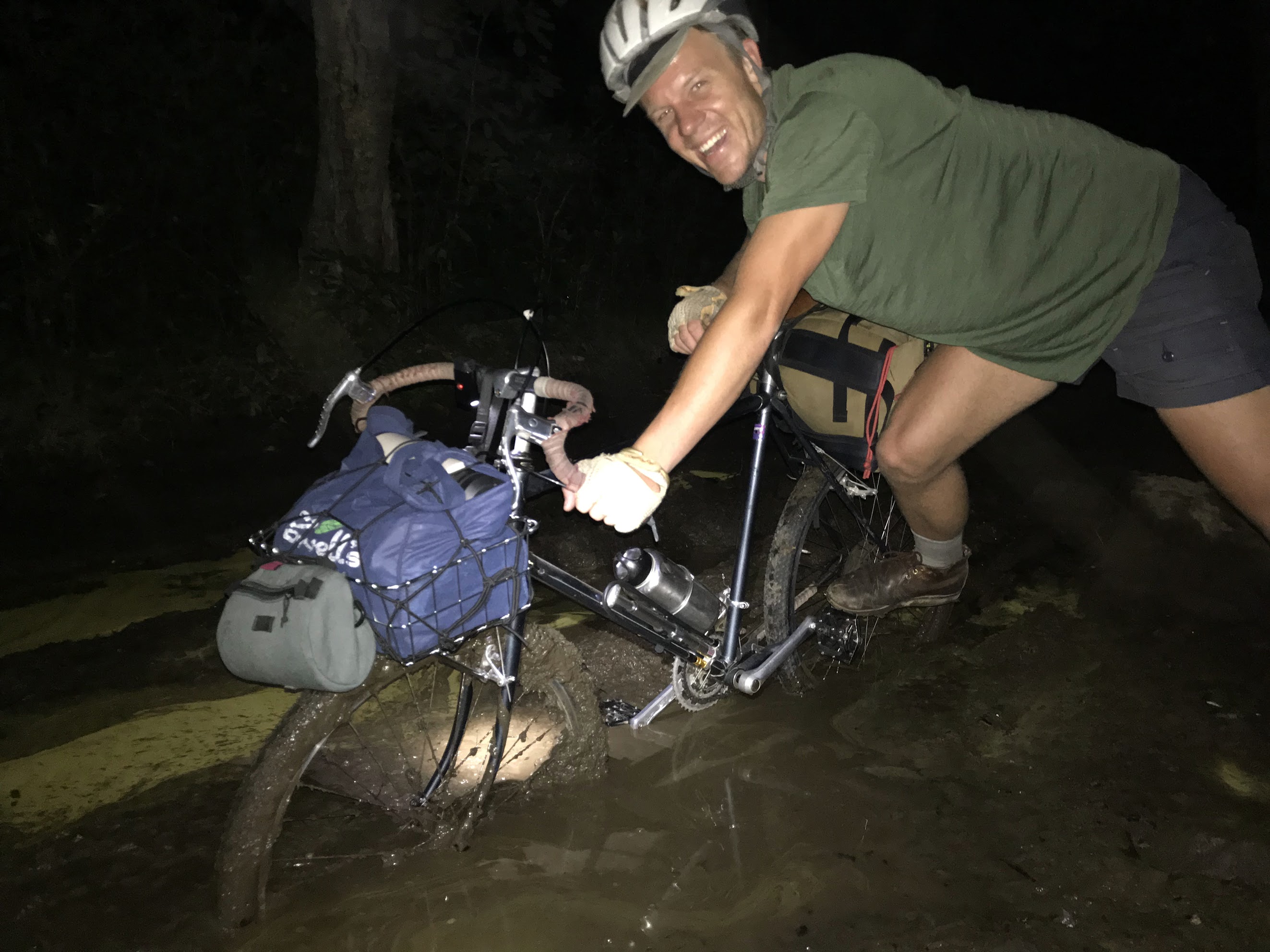 Trevor Borden laughing while dragging a loaded bicycle through mud at night on a bikepacking trip
